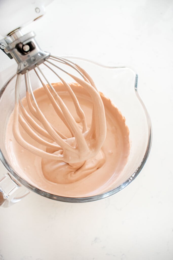 fluffy chocolate marshmallow fluff in a glass mixing bowl with a whisk on a marble counter.