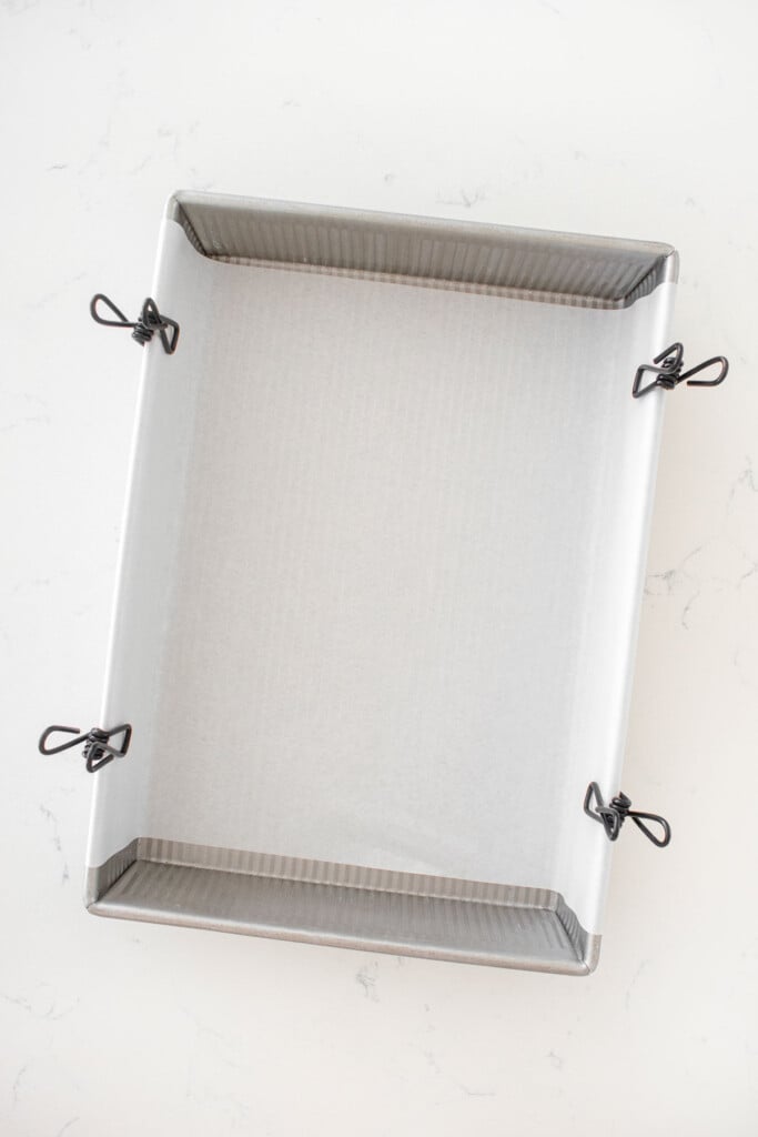 9x13 inch baking pan with parchment paper on a white marble counter.