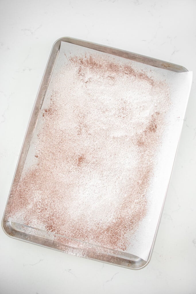 sifted powdered sugar and cocoa on a baking sheet with parchment paper on a marble counter.