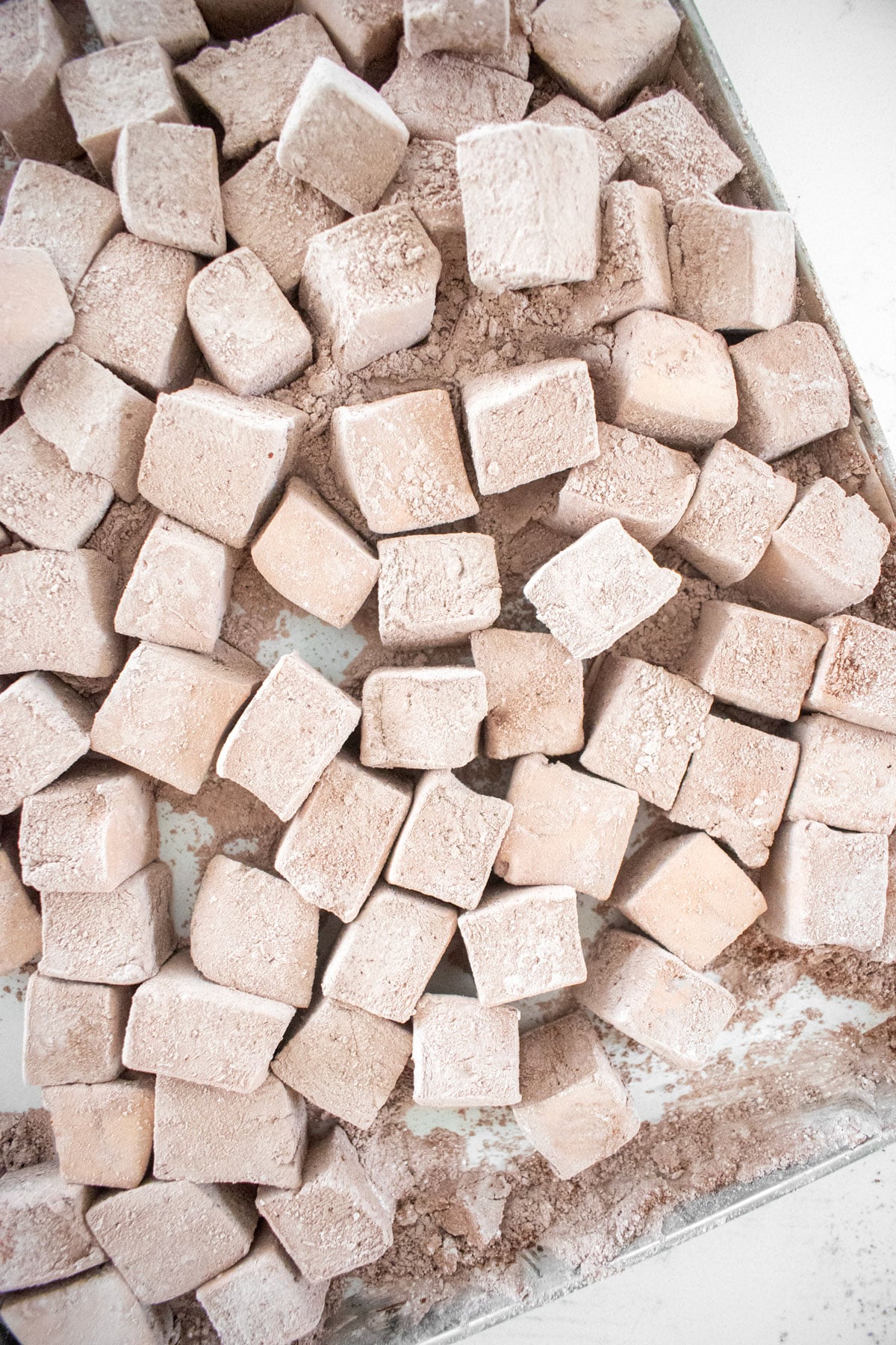 homemade chocolate marshmallows cut into mini squares on a baking sheet on a marble counter.