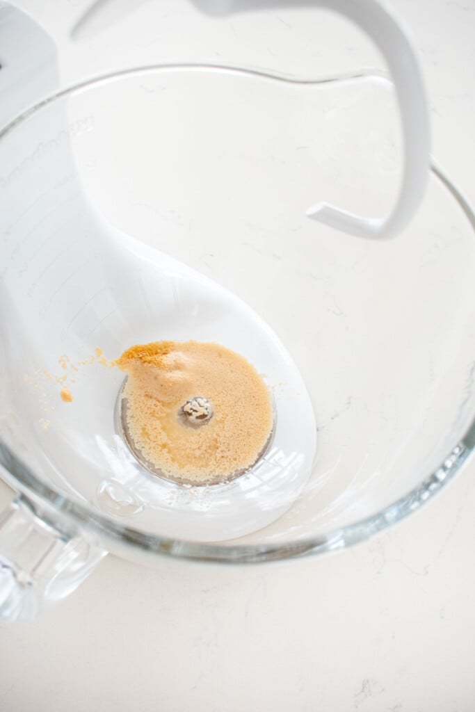 yeast and water in a glass mixing bowl on aw white marble counter.