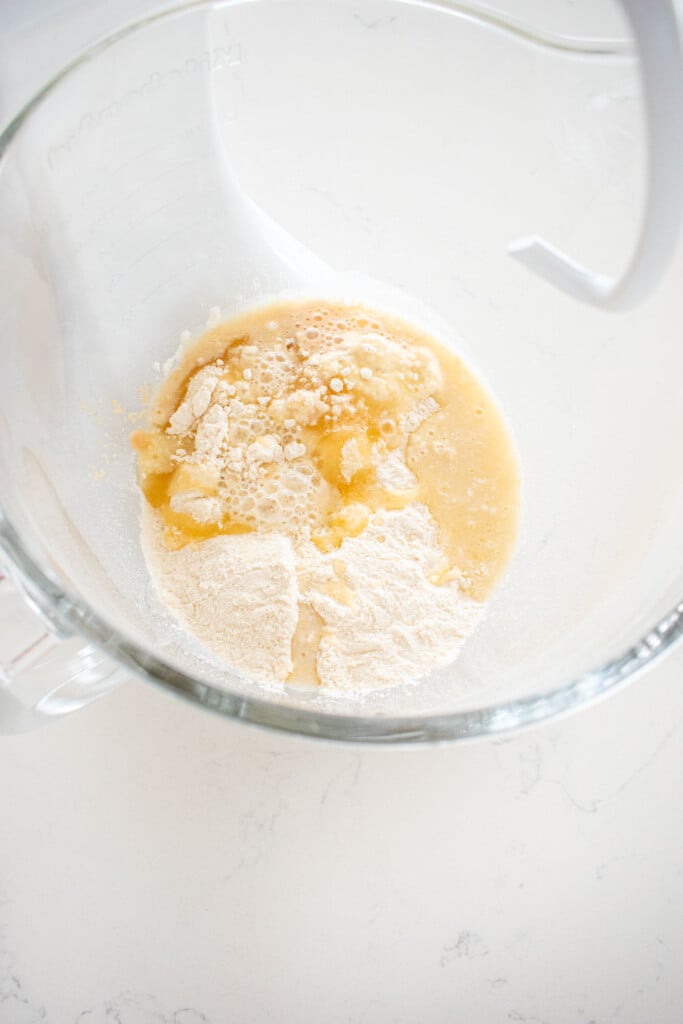 ingredients for honey butter dinner rolls in a glass mixing bowl on a white marble counter.
