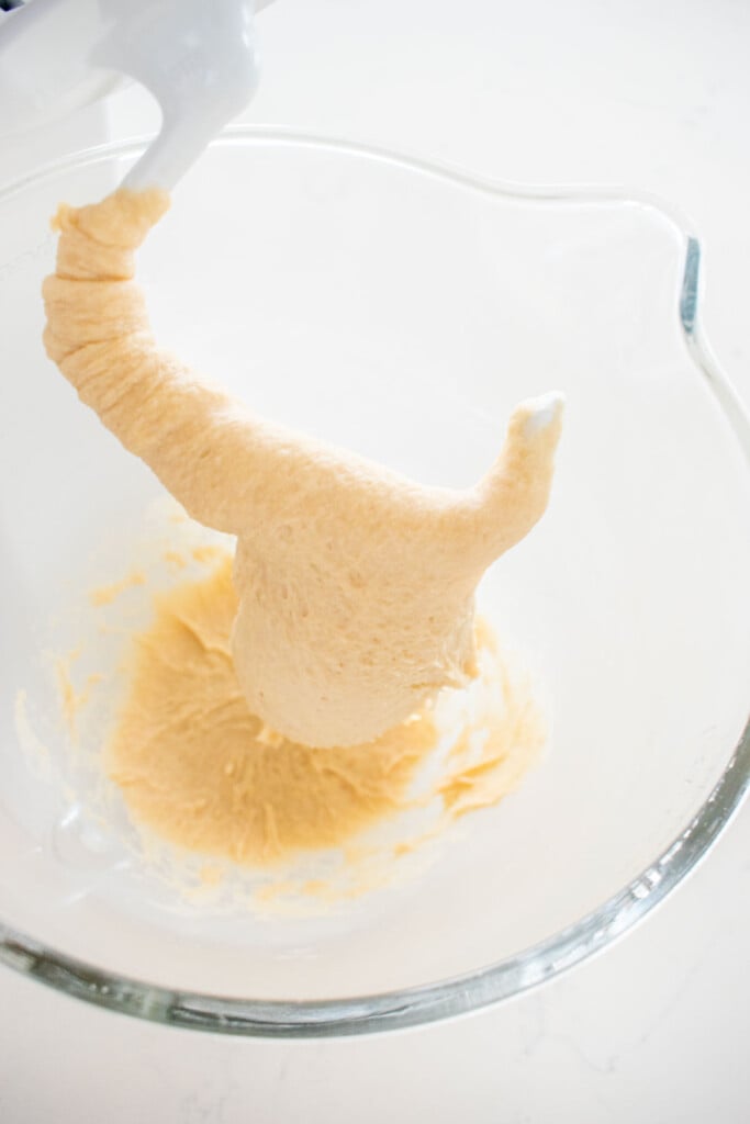 honey butter cinnamon roll dough in a glass mixing bowl on a white marble counter.