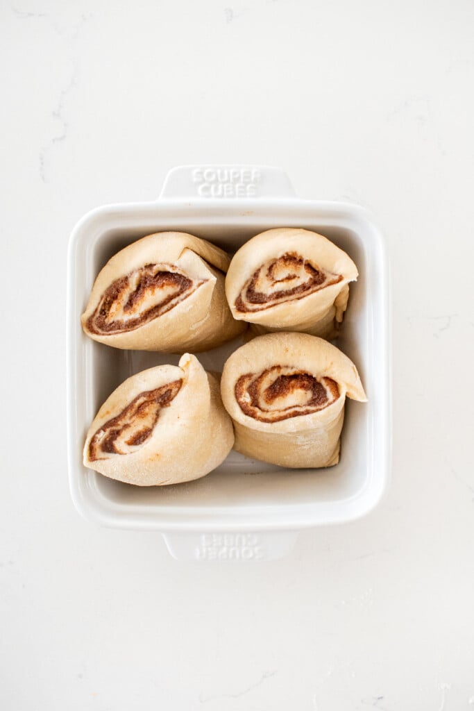 raw honey butter cinnamon rolls in a white baking dish on a marble counter.