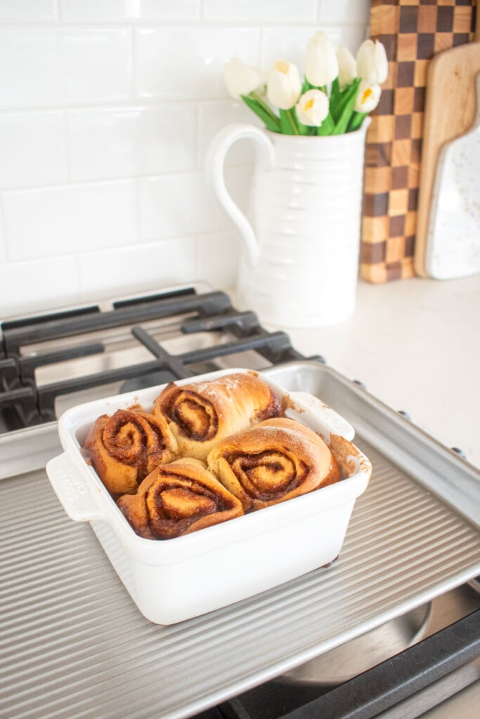 small batch honey butter cinnamon rolls in a white baking dish on a sheet pan sitting on the stovetop cooling.