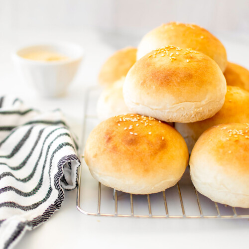 soft white hamburger buns on a cooling rack on a white marble counter.