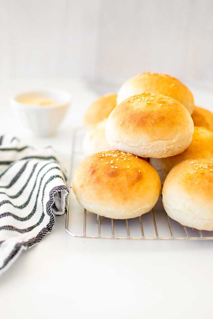 soft white hamburger buns on a cooling rack on a white marble counter.