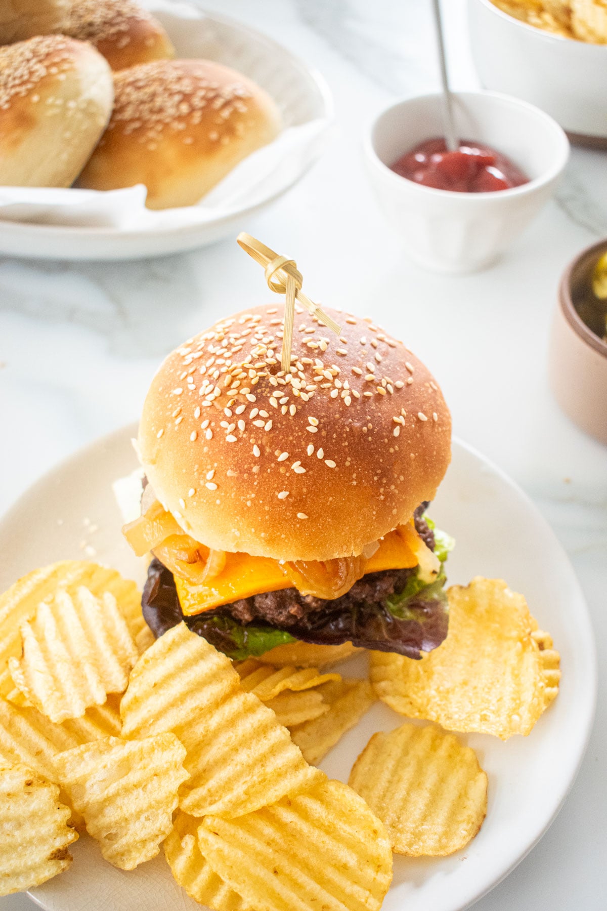cheeseburger made on a soft white hamburger bun on a plate with chips on a marble counter.