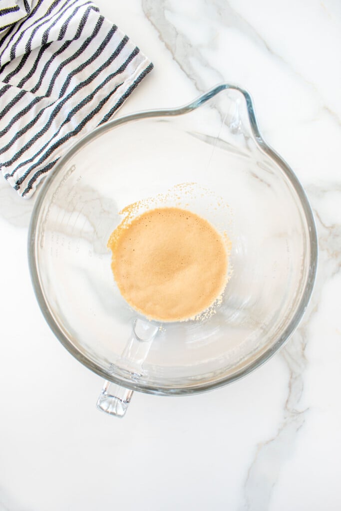yeast and water in a glass mixing bowl on a marble counter.