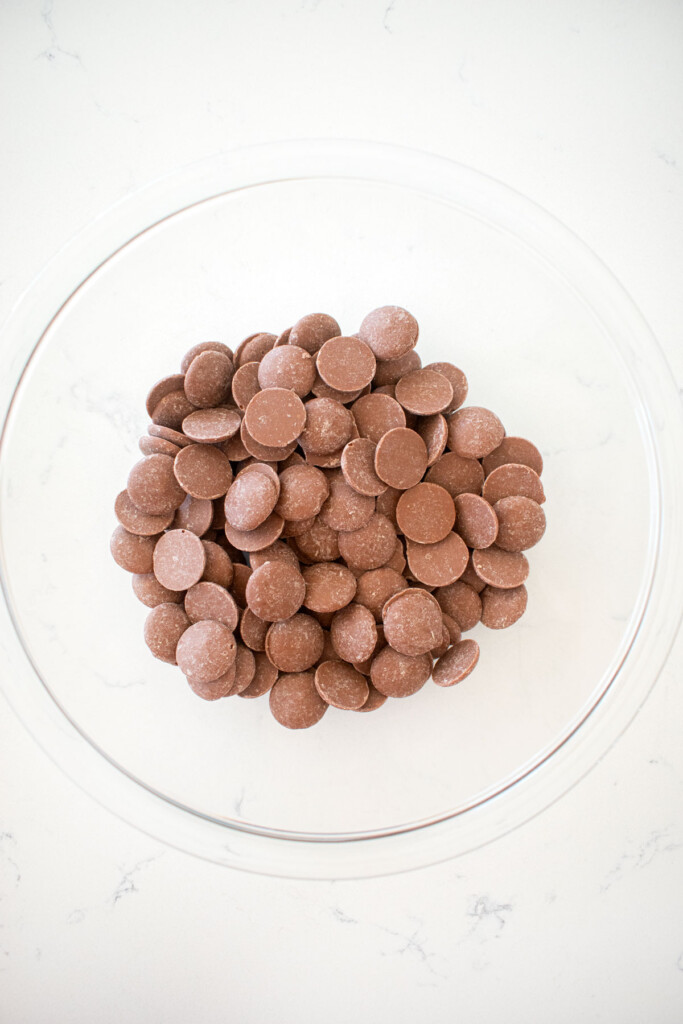 milk chocolate in a glass mixing bowl on a white marble counter.