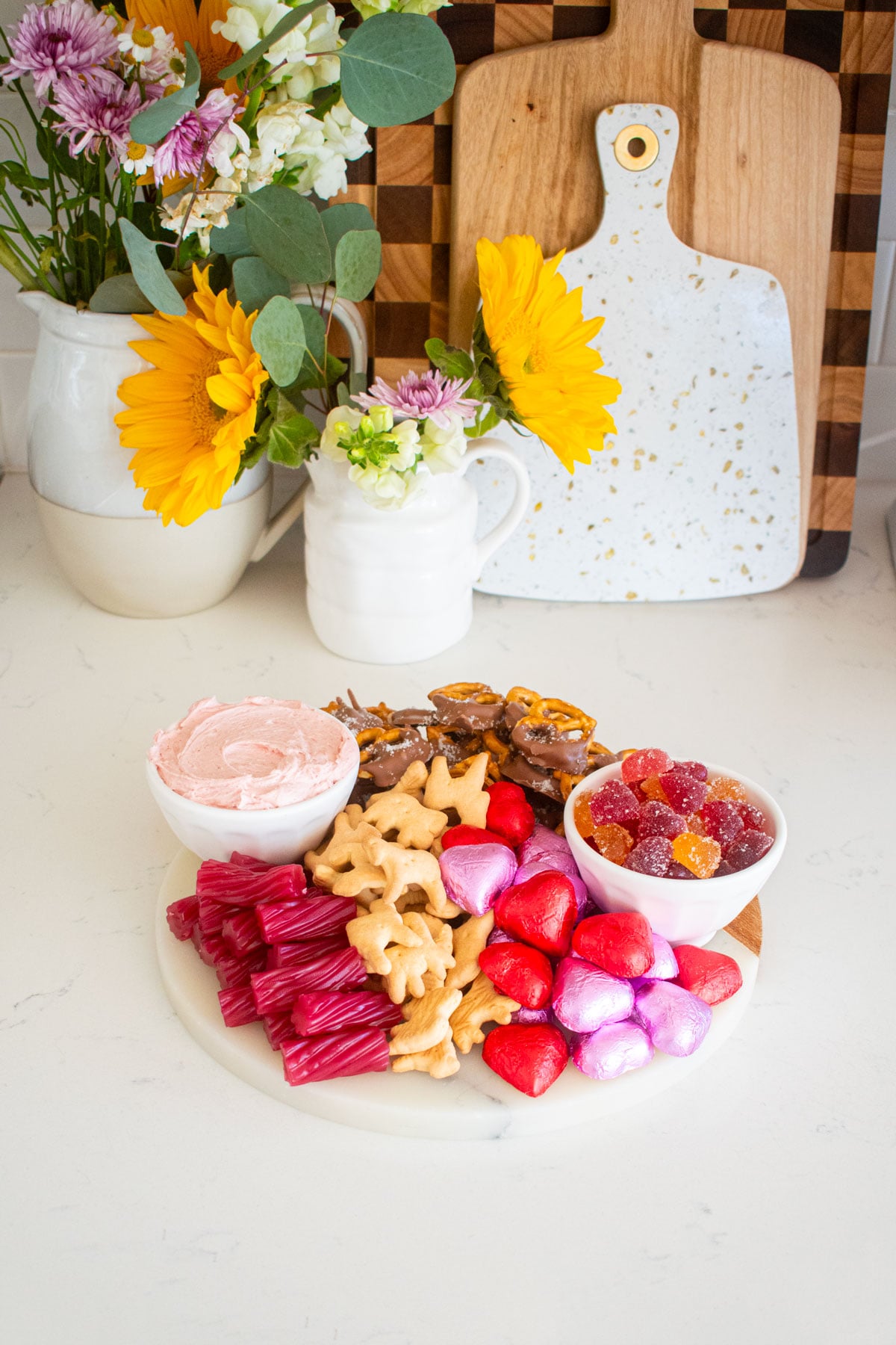 valentine's day charcuterie board on a white marble counter with fresh flowers.