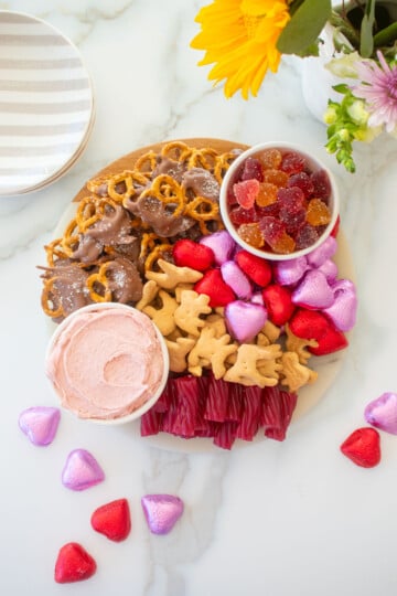 valentine's day charcuterie board on a white marble counter with fresh flowers.