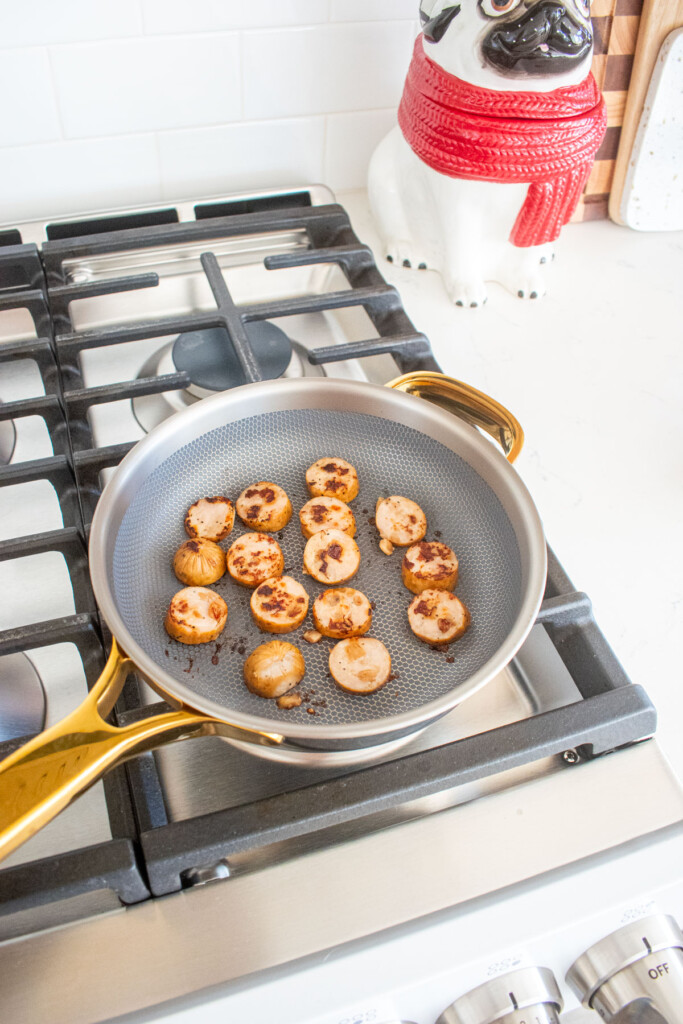 sliced chicken sausages sliced browning in a skillet on a stovetop.