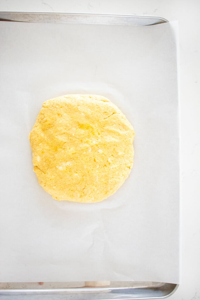 citrus scones dough formed into a round disk on a baking sheet with parchment paper.