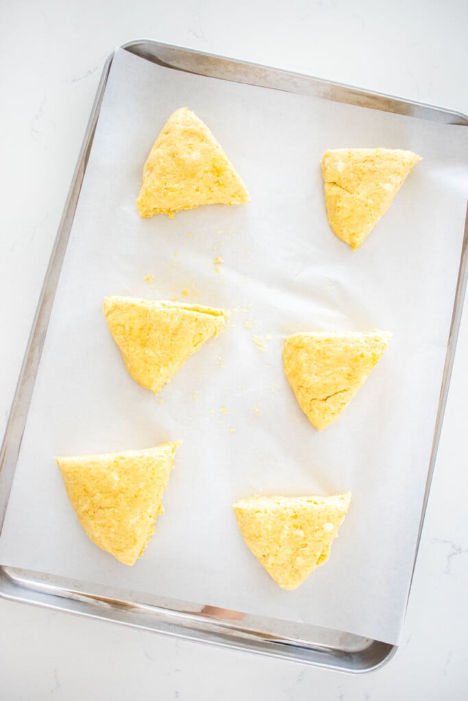 citrus scones dough cut into 6 triangles spread out evenly on a baking sheet on a white marble counter.