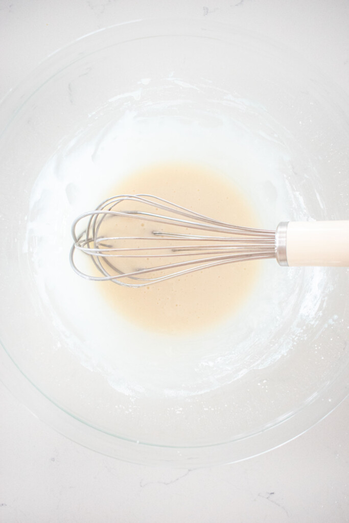 glaze in a glass mixing bowl with a whisk on a white marble counter.