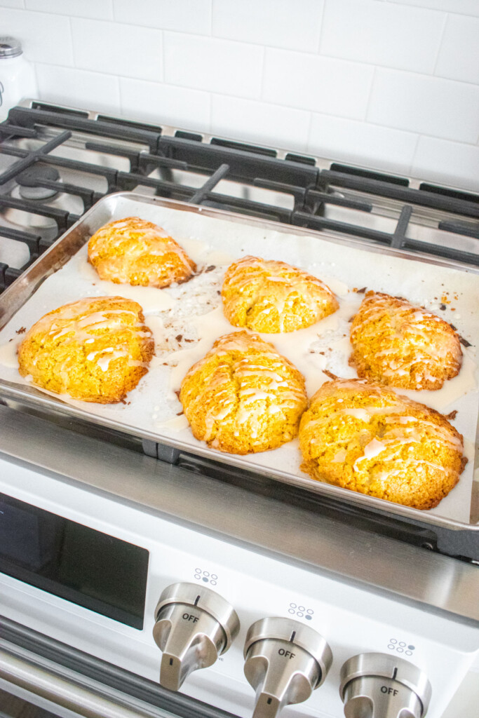 citrus scones with glaze on a baking sheet on top of an oven.