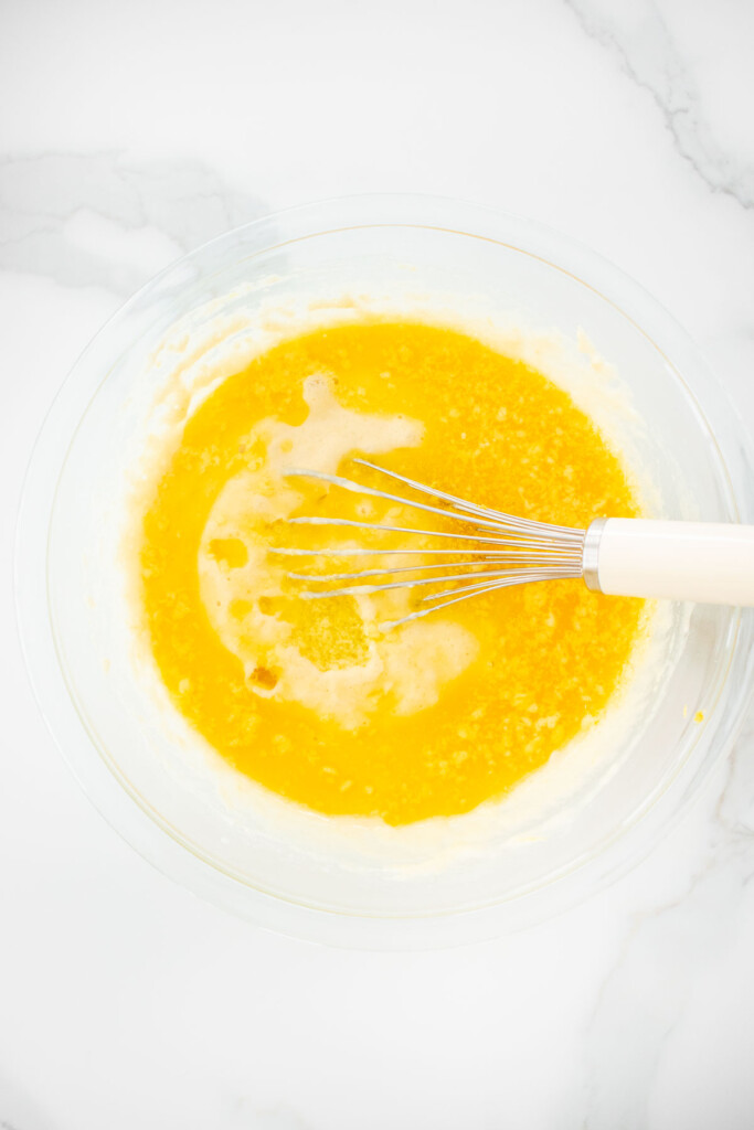 meyer lemon pancake batter being mixed with a whisk in a glass bowl on a white marble counter.