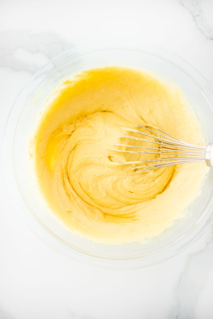 meyer lemon pancake batter being mixed with a whisk in a glass bowl on a white marble counter.