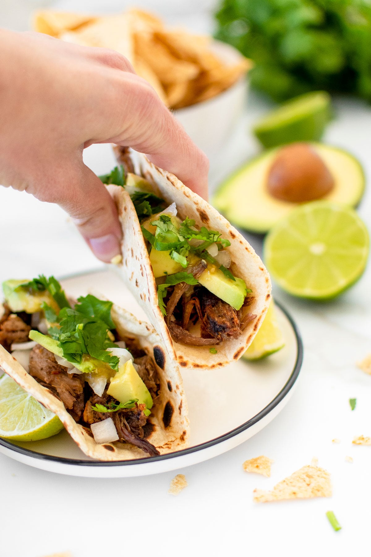 woman grabbing a slow cooker pulled pork street taco off a plate.