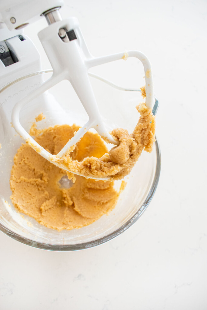 creamed butter and sugar in a glass stand mixing bowl on a white marble counter.