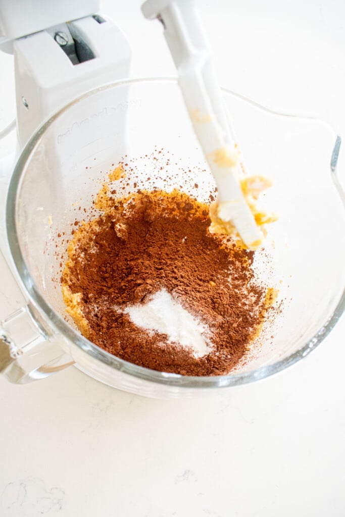 ingredients for thin mint biscotti dough in a glass stand mixing bowl on a white marble counter.