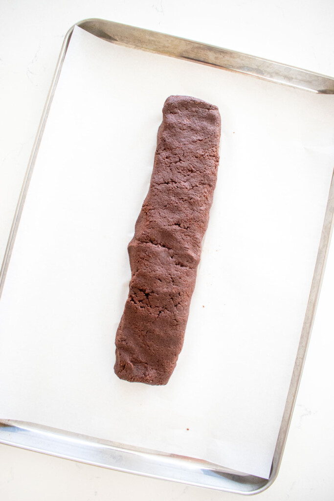 chocolate biscotti dough log on a baking sheet on a white marble counter.