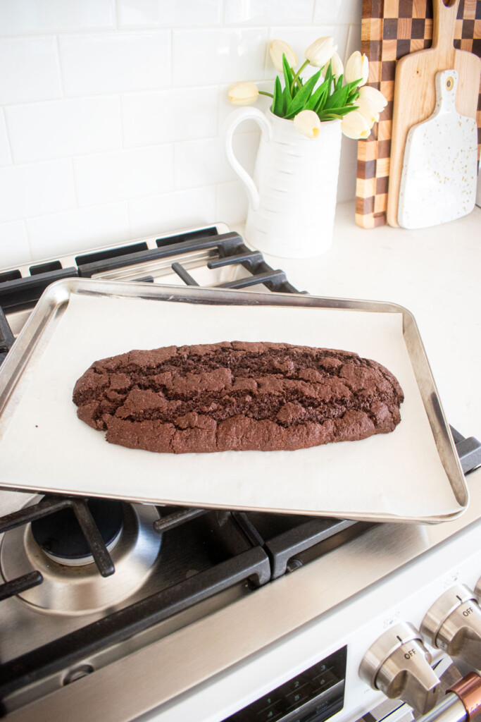 baked biscotti chocolate log on a baking sheet cooling on top of an oven.
