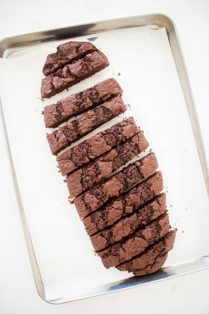 chocolate biscotti cut into slices on a baking sheet on a marble counter.