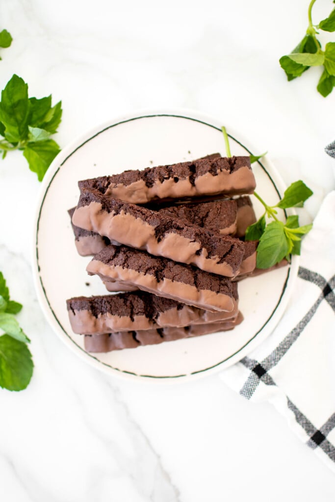 plate of thin mint biscotti on a marble table with fresh mint leaves.