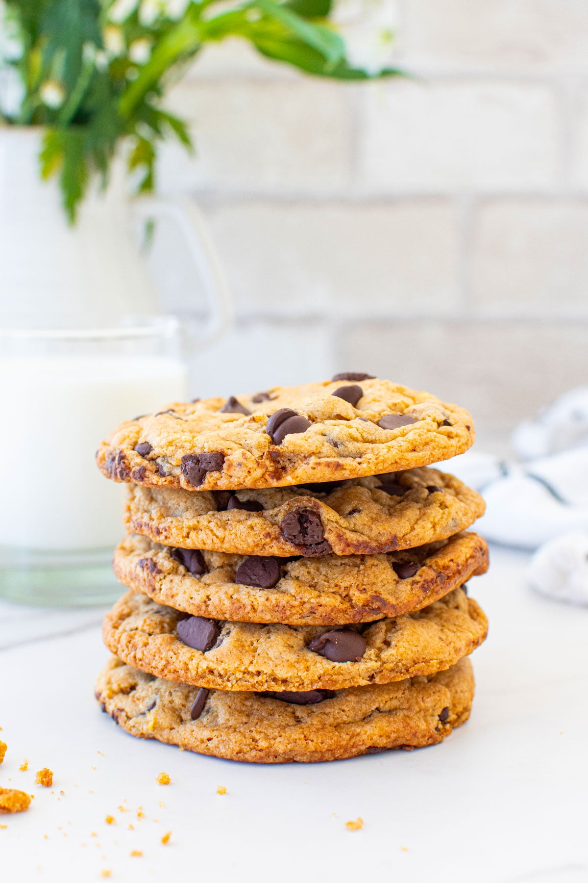 stack of vegan banana chocolate chip cookies on a marble counter with a glass of milk and fresh flowers.