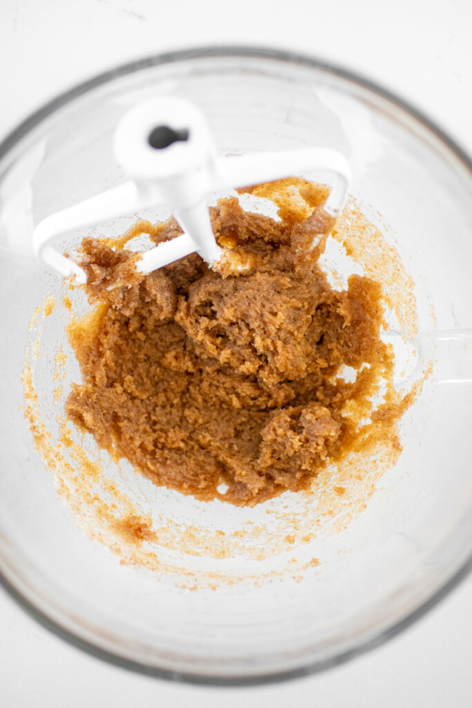 creamed coconut oil and sugar in a glass mixing bowl on a marble counter.