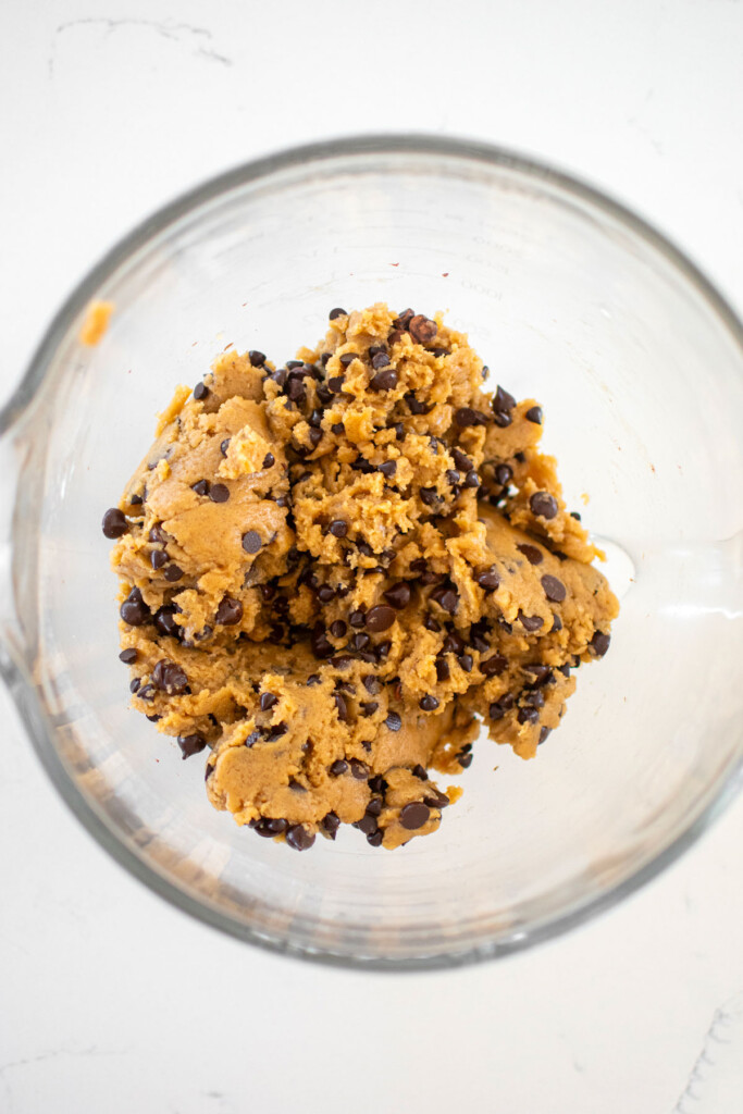 vegan banana chocolate chip cookie dough in a glass mixing bowl on a marble counter.