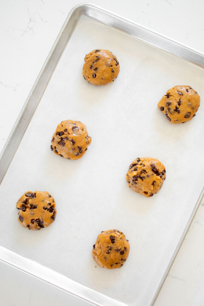 vegan banana chocolate chip cookie dough balls on a baking sheet on a marble counter.