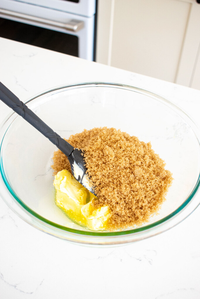 butter and brown sugar in a glass mixing bowl on a white marble counter.
