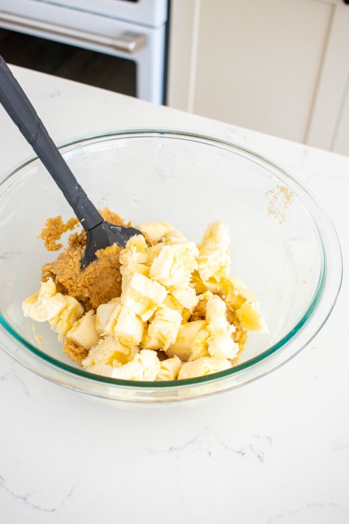 bananas and creamed butter and sugar in a glass mixing bowl on a white marble counter.