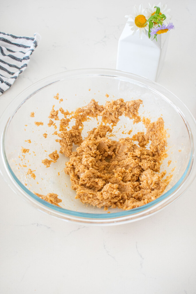 creamed butter and brown sugar in a glass mixing bowl on a marble counter with fresh flowers.