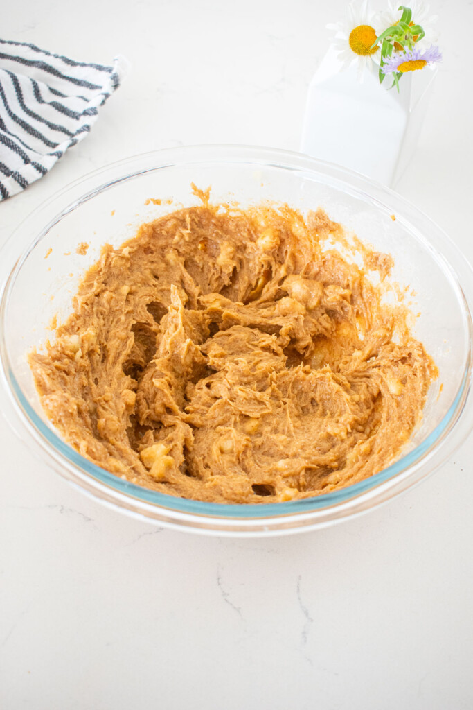 creamed wet ingredients for almond butter banana bread in a glass mixing bowl on a marble counter.