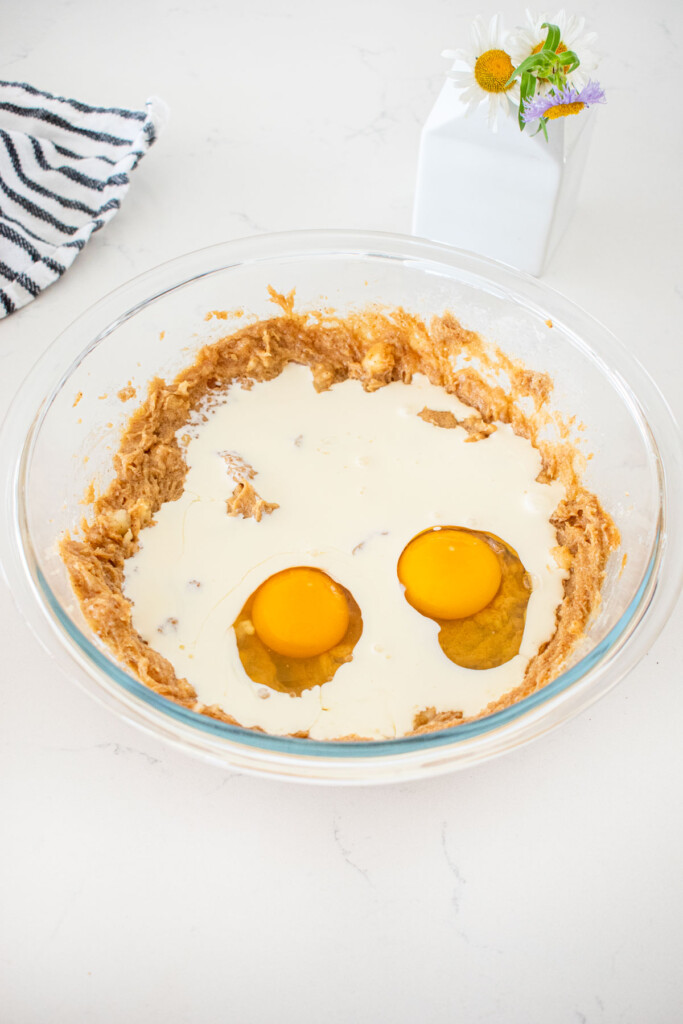 heavy cream and eggs added to wet ingredients for almond butter banana bread batter in a glass mixing bowl on a marble counter.