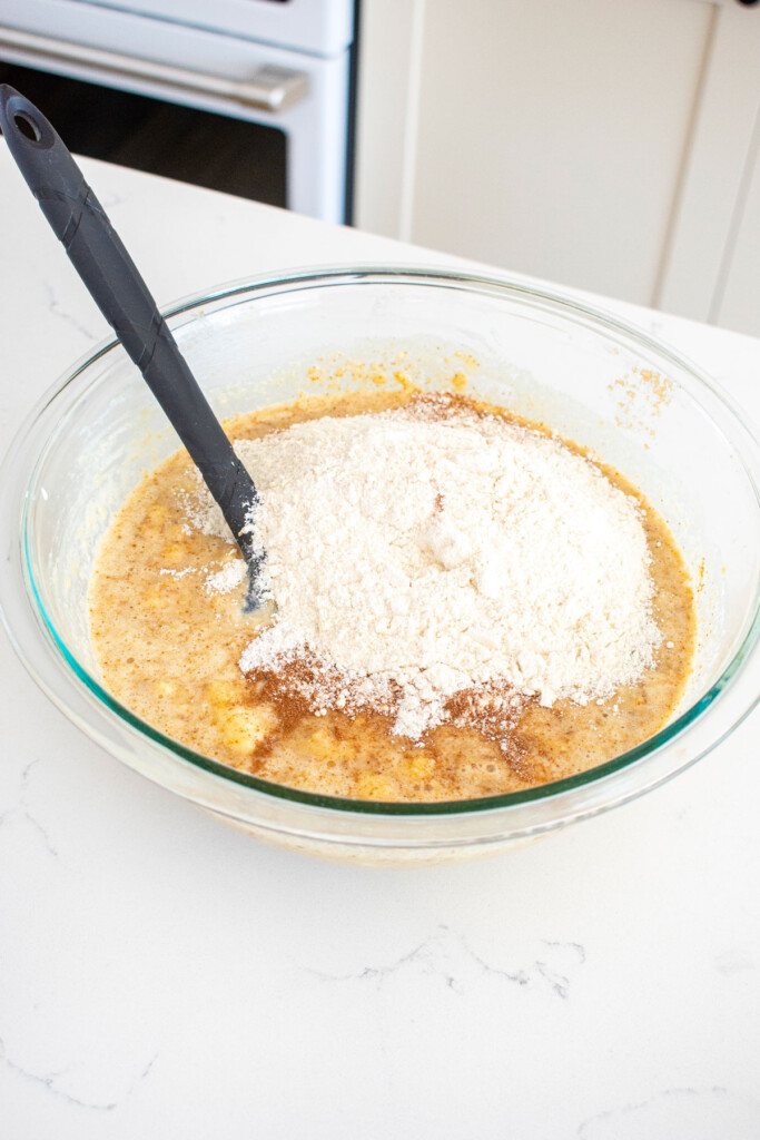 ingredients for almond butter banana bread in a glass bowl on a white marble counter.