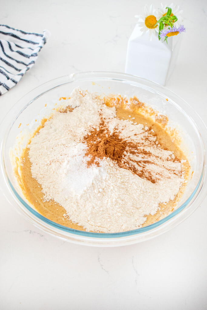 dry ingredients being added to wet ingredients for almond butter banana bread batter in a glass mixing bowl on a marble counter.