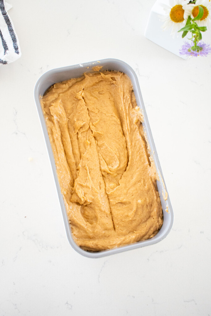 loaf pan with almond butter banana bread batter in it on a marble counter.