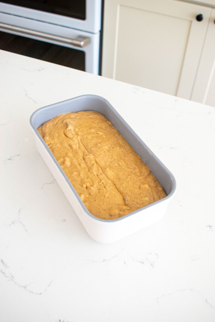 almond butter banana bread batter in a loaf pan on a white marble counter.