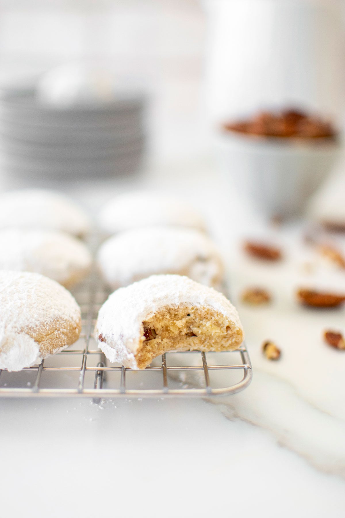Cinnamon Pecan Kourambiethes (Greek Butter Cookies) on a cooling rack on a white marble countertop.