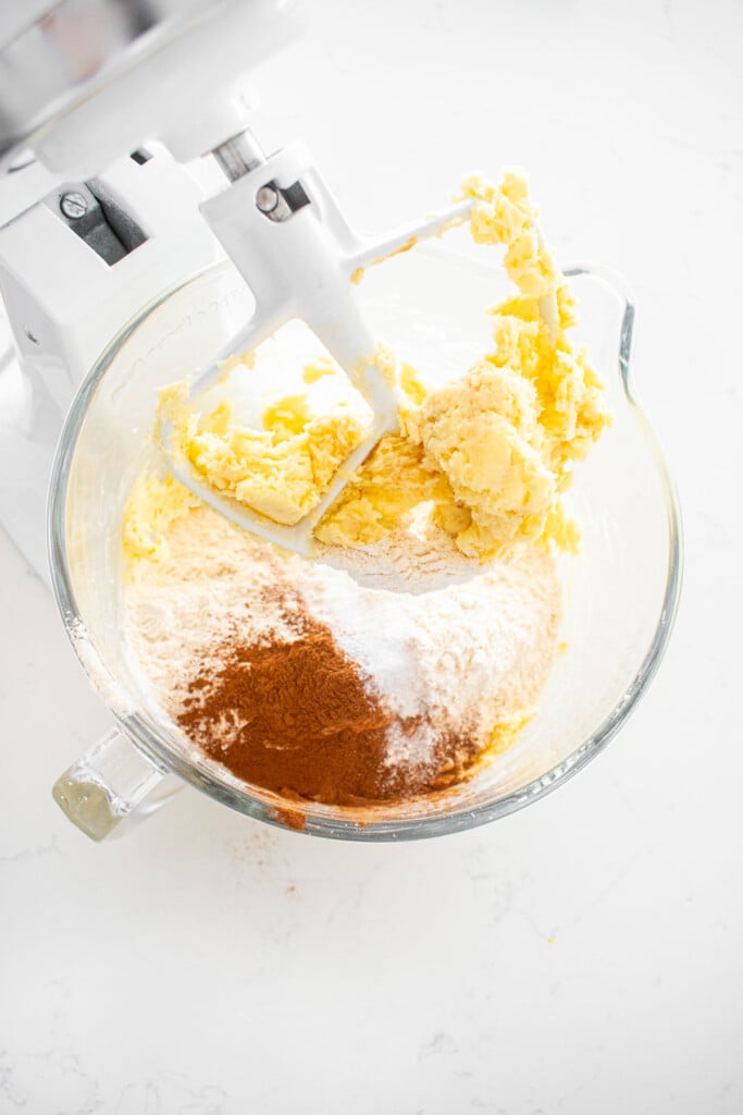 dry ingredients for cinnamon pecan greek butter cookies on top of creamed butter and sugar in a glass stand mixer on a white marble counter.