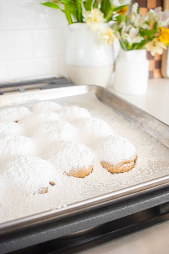 cinnamon pecan greek butter cookies with powdered sugar on top on a baking sheet sitting on top of an oven.