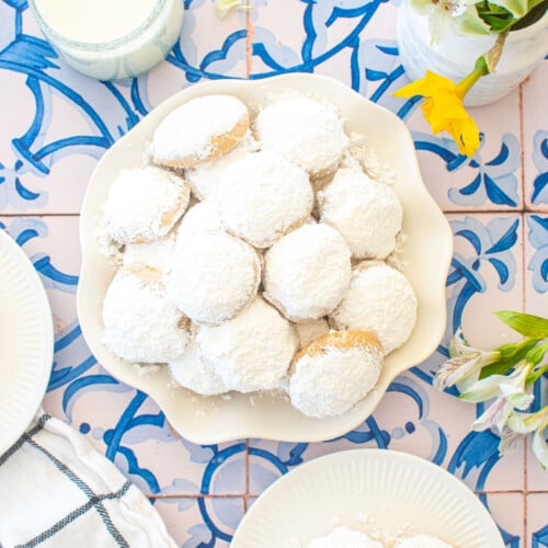 ruffle plate of cinnamon pecan greek butter cookies on a blue tile table with fresh flowers.
