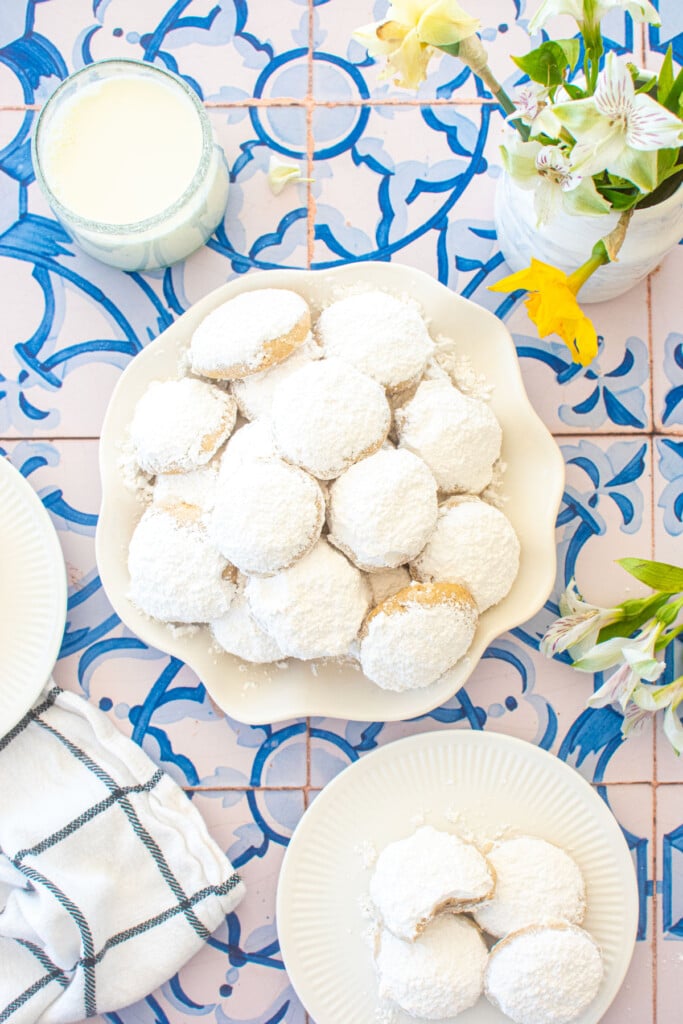 ruffle plate of cinnamon pecan greek butter cookies on a blue tile table with fresh flowers.