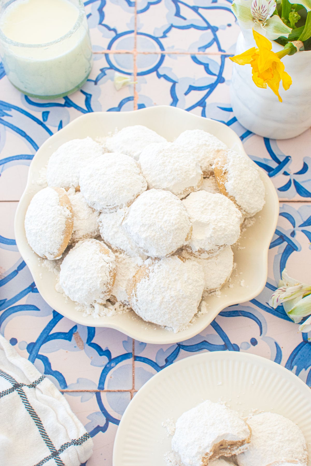 ruffle plate of cinnamon pecan greek butter cookies on a blue tile table with fresh flowers.