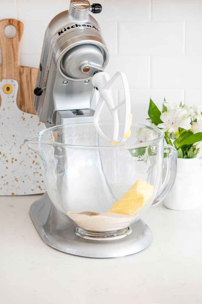 glass stand mixing bowl with butter sugar and vanilla on a white marble counter with fresh flowers.